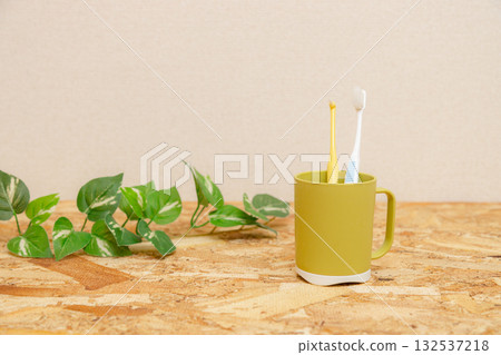 Two toothbrushes in a cup placed on a wooden table. Single-tufted toothbrushes. Two toothbrushes in a cup placed on a wooden table. Single-tufted toothbrushes. 132537218