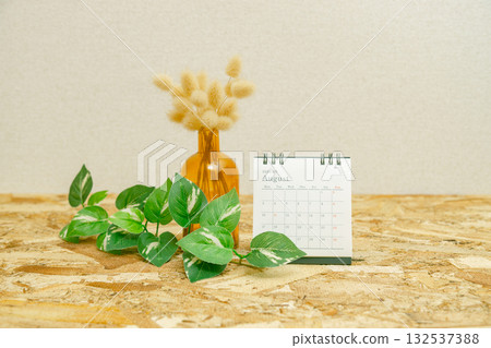 August 2026 desk calendar and dried flowers stock photo. There is a potted plant on an OSB plywood table. 132537388