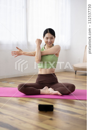 Middle-aged woman stretching while looking at her smartphone Middle-aged woman stretching while looking at her smartphone 132537730