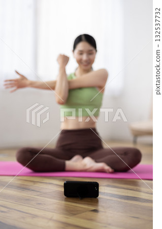 A smartphone placed in front of a woman taking an online yoga class at home 132537732