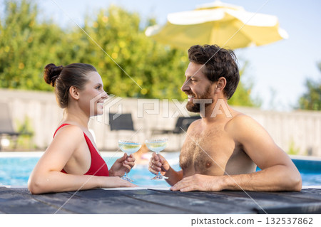 Nice couple in an open swimming pool with glasses with drink in hands Nice couple in an open swimming pool with glasses with drink in hands 132537862
