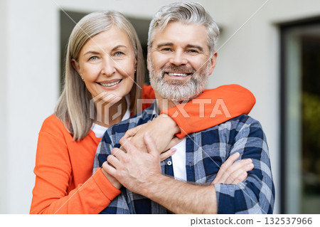Cute woman in orange shirt hugging her husband and smiling nicely Cute woman in orange shirt hugging her husband and smiling nicely 132537966