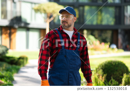 Man gardener posing confidently in green courtyard near modern building Man gardener posing confidently in green courtyard near modern building 132538018