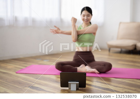 一位在瑜珈墊上伸展身體的女士面前放著一台平板電腦。 132538070
