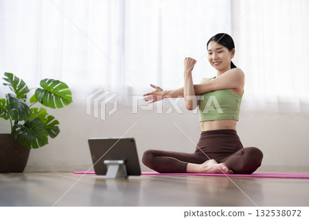 Middle-aged woman stretching while looking at a tablet Middle-aged woman stretching while looking at a tablet 132538072