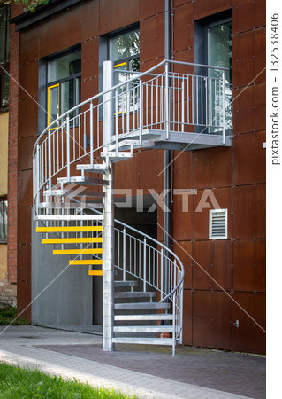 Modern exterior spiral staircase made of galvanized steel with yellow safety markings on the steps 132538406
