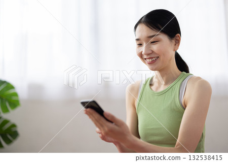 一位身穿瑜珈服的中年婦女正在操作智慧型手機，帶著微笑。 132538415