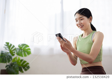 A middle-aged woman wearing yoga wear operating a smartphone and smiling 132538420
