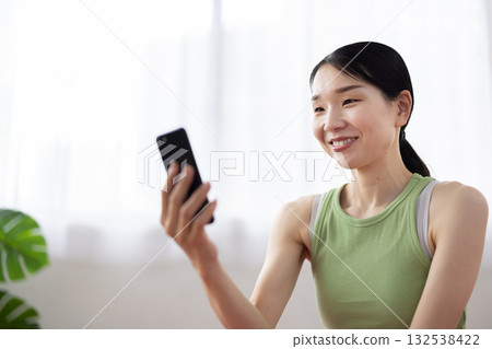 A middle-aged woman wearing yoga wear operating a smartphone and smiling A middle-aged woman wearing yoga wear operating a smartphone and smiling 132538422