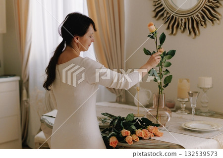 Woman arranging peach roses, decorating dining table at home 132539573