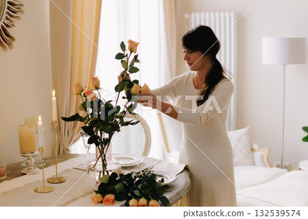 Woman arranging fresh roses on dining table 132539574