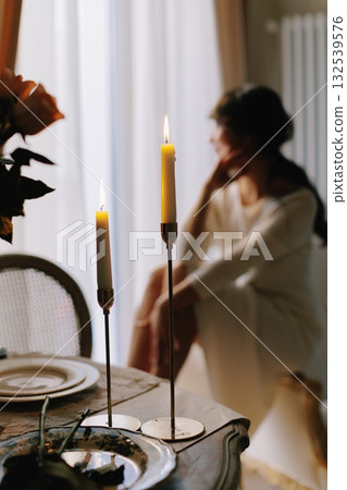 Candles illuminating a pensive woman at dinner table 132539576