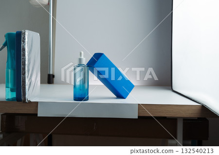 Behind-the-scenes view of product photography setup with softbox, white background, and reflector propped on a spray bottle, mobile photo. Concept of studio, lighting, photography, setup. 132540213