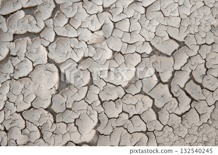 Dry cracked soil surface forms abstract natural pattern under sunlight. Texture shows drought effect and desiccation process symbolizing heat, climate change and environmental stress 132540245
