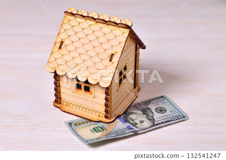 A small wooden house-piggy bank and a banknote 100 dollars on a wooden background A small wooden house-piggy bank and a banknote 100 dollars on a wooden background 132541247