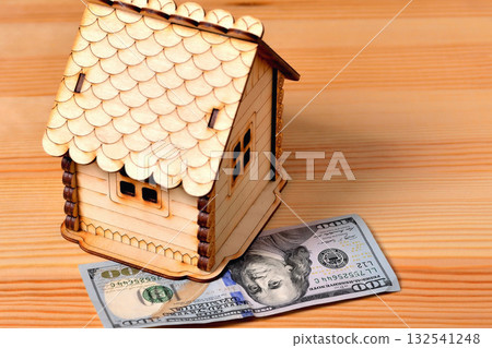 A small wooden house-piggy bank and a banknote 100 dollars on a wooden background 132541248