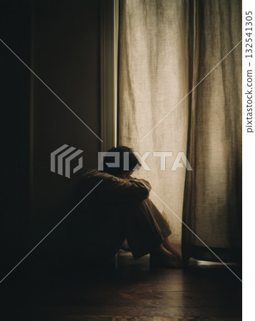 Silhouetted figure sits alone by a window in low light. Soft curtain, shadows, and quiet emotion convey solitude, reflection, and mental stillness Silhouetted figure sits alone by a window in low light. Soft curtain, shadows, and quiet emotion convey solitude, reflection, and mental stillness 132541305