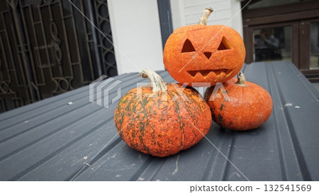 Three pumpkins arranged outdoors with one carved into a jack-o'-lantern featuring a smiling face. The image represents Halloween decoration, autumn celebration, and seasonal creativity 132541569