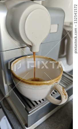 Fresh espresso being poured from a coffee machine into a ceramic cup in a cozy kitchen setting. The image represents morning routine, caffeine boost, and the art of coffee making Fresh espresso being poured from a coffee machine into a ceramic cup in a cozy kitchen setting. The image represents morning routine, caffeine boost, and the art of coffee making 132541572