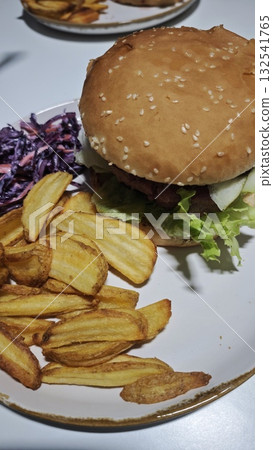 Juicy burger with lettuce and pickles served on a plate with crispy fries and purple coleslaw. The image represents comfort food, casual dining, and homemade fast food enjoyment 132541765