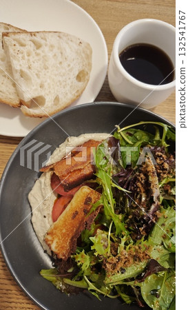 Fresh salad with grilled halloumi cheese, greens, and hummus served with rustic bread and black coffee. The image represents healthy eating, cafe dining, and balanced modern lifestyle Fresh salad with grilled halloumi cheese, greens, and hummus served with rustic bread and black coffee. The image represents healthy eating, cafe dining, and balanced modern lifestyle 132541767