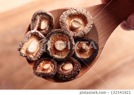 Dried organic shiitake mushrooms in a wooden spoon held by a hand. Top view 132541921
