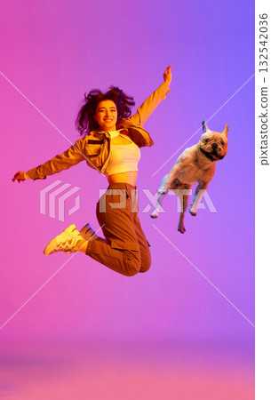 Young woman and dog jumping in colorful studio light representing sport and joy Young woman and dog jumping in colorful studio light representing sport and joy 132542036