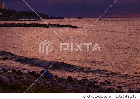 A man watches the waves crashing on the beach at sunset A man watches the waves crashing on the beach at sunset 132542135