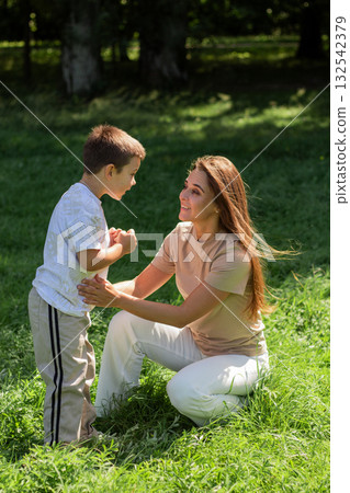 Young Caucasian mother laughs giggling son across sunny park lawn. Dynamic image radiates pure joy, energy, and fun of outdoor playtime together. Young Caucasian mother laughs giggling son across sunny park lawn. Dynamic image radiates pure joy, energy, and fun of outdoor playtime together. 132542379