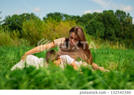 Mom and her boy kid spending time together on nature and reading interesting book about dinosaurs. Quality time with child. 132542380
