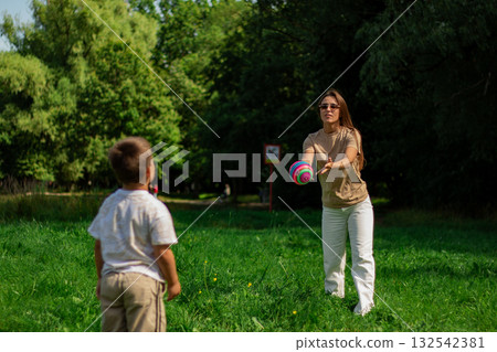 Active lifestyle of mom and son. Energetic scene of mother and boy running and kicking ball on sunny day. Ideal for themes of health, fitness, sports, and active living for all ages. Active lifestyle of mom and son. Energetic scene of mother and boy running and kicking ball on sunny day. Ideal for themes of health, fitness, sports, and active living for all ages. 132542381