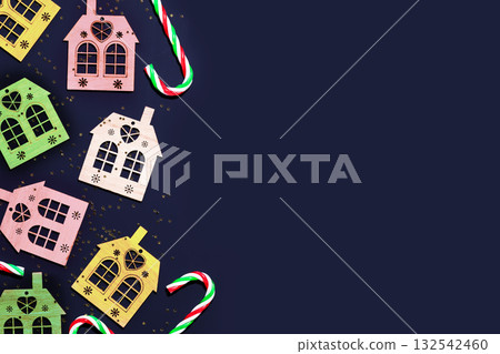 Christmas background with decorative, multicolored, wodden houses, sweets and golden confetti on a deep blue background with place for text. Merry Christmas composition, flat lay Christmas background with decorative, multicolored, wodden houses, sweets and golden confetti on a deep blue background with place for text. Merry Christmas composition, flat lay 132542460