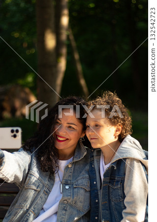Mother making selfie together with her son. Taking selfie on smartphone. Smiling happy young family make photos outside in park to memorize moment. Mother making selfie together with her son. Taking selfie on smartphone. Smiling happy young family make photos outside in park to memorize moment. 132542723