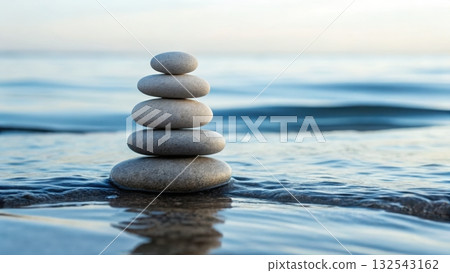 Smooth balanced stones carefully stacked on peaceful shoreline with gentle waves in the background 132543162
