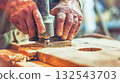 Weathered hands guide power tool over wooden surface, surrounded by sawdust in workshop setting. Concept of skill, precision and dedication of modern woodworking. Perfect for DIY, craftsmanship themes 132543703