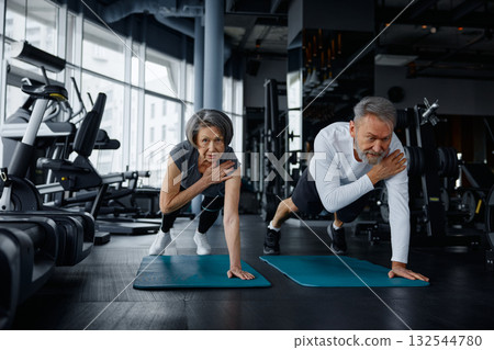 Mature man and woman are doing exercises on yoga mats in a gym Mature man and woman are doing exercises on yoga mats in a gym 132544780
