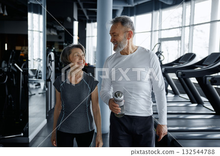 A man and a woman are leisurely walking together in a gym facility A man and a woman are leisurely walking together in a gym facility 132544788