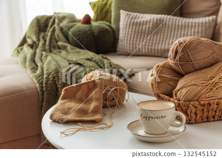 Cozy Living Room with Yarn, Pumpkins, Pillows and Cup of Cappuccino on White Table Cozy Living Room with Yarn, Pumpkins, Pillows and Cup of Cappuccino on White Table 132545152