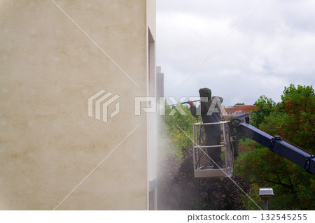 Unrecognizable man cleaning facade surface from lifting platform with high pressure stream of water Unrecognizable man cleaning facade surface from lifting platform with high pressure stream of water 132545255