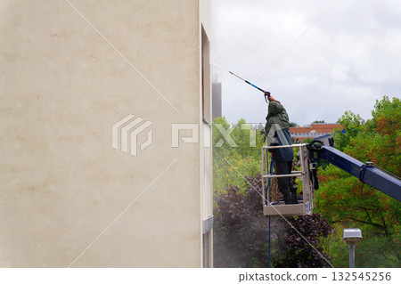Unrecognizable man cleaning facade surface from lifting platform with high pressure stream of water 132545256