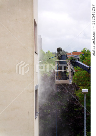 Unrecognizable man cleaning facade surface from lifting platform with high pressure stream of water Unrecognizable man cleaning facade surface from lifting platform with high pressure stream of water 132545257