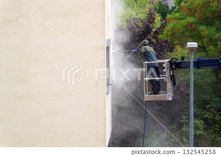 Unrecognizable man cleaning facade surface from lifting platform with high pressure stream of water 132545258