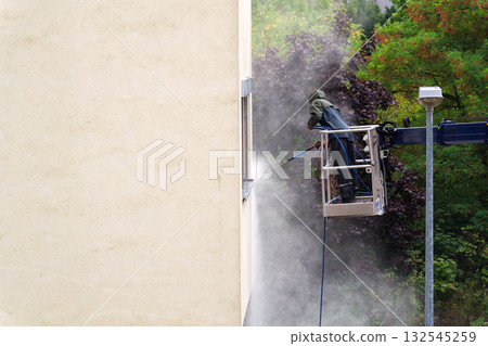 Unrecognizable man cleaning facade surface from lifting platform with high pressure stream of water 132545259