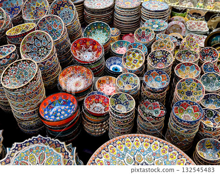 Colorful handmade ceramic bowls with traditional oriental patterns displayed at a market. Souvenir and decor concept. Top view. 132545483