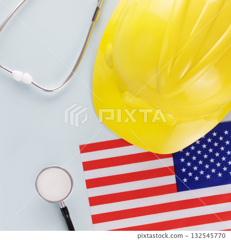 Medical care and insurance of workers in America. American flag, stethoscope and hardhat on a blue background. Labor safety and right at Workplace in United States Medical care and insurance of workers in America. American flag, stethoscope and hardhat on a blue background. Labor safety and right at Workplace in United States 132545770