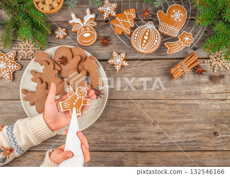 Decorating Christmas gingerbread man cookie white icing, hands holding piping bag over festive cookies on wooden table with cinnamon sticks, fir branches, cozy holiday atmosphere, top view Decorating Christmas gingerbread man cookie white icing, hands holding piping bag over festive cookies on wooden table with cinnamon sticks, fir branches, cozy holiday atmosphere, top view 132546166