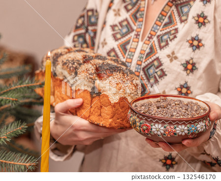 Traditional Ukrainian Christmas kutia and homemade bread in hands of woman wearing embroidered shirt, festive ritual meal of Holy Supper candle fir branches, authentic ethnic celebration scene Traditional Ukrainian Christmas kutia and homemade bread in hands of woman wearing embroidered shirt, festive ritual meal of Holy Supper candle fir branches, authentic ethnic celebration scene 132546170