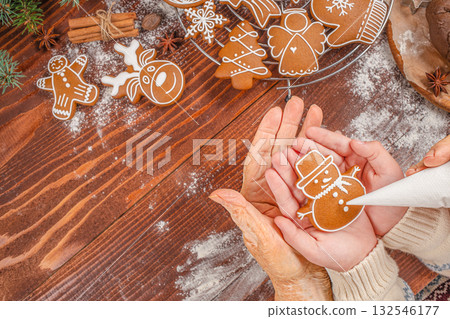 Generations baking together elderly and young hands decorating snowman gingerbread cookie with icing on wooden table, family Christmas tradition, festive atmosphere, top view Generations baking together elderly and young hands decorating snowman gingerbread cookie with icing on wooden table, family Christmas tradition, festive atmosphere, top view 132546177