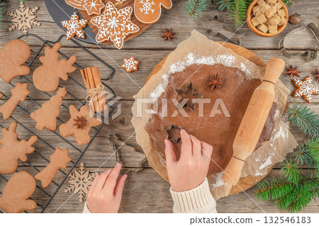 Christmas cookie making process with hands cutting shapes from gingerbread dough using cutters on rustic wooden table, holiday baking concept, spices, and decorated cookies, top view copy space Christmas cookie making process with hands cutting shapes from gingerbread dough using cutters on rustic wooden table, holiday baking concept, spices, and decorated cookies, top view copy space 132546183