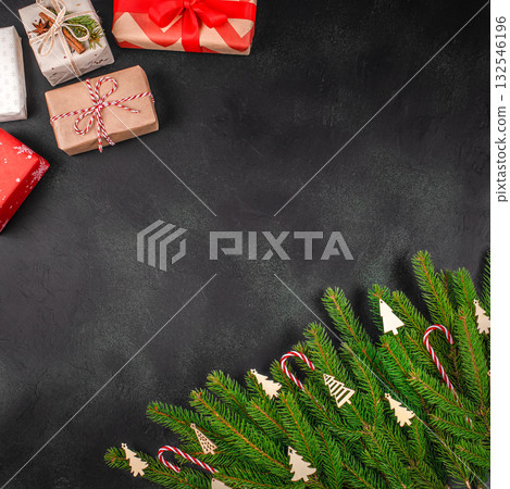 Christmas composition with gift boxes wrapped in craft and red paper, fir branches with wooden decorations and candy canes on dark background, festive flat lay with copy space 132546196